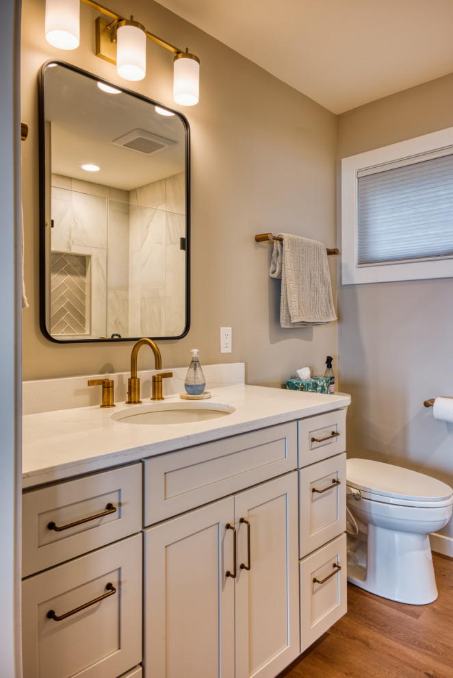 Mid-sized transitional 3/4 vinyl floor, brown floor and single-sink bathroom photo with shaker cabinets, white cabinets, a two-piece toilet, beige walls, quartzite countertops, white countertops and a built-in vanity