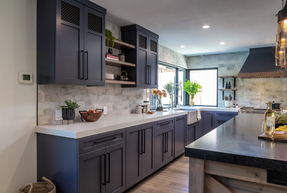This is an example of a large industrial l-shaped eat-in kitchen in San Francisco with an undermount sink, shaker cabinets, black cabinets, granite benchtops, stone slab splashback, stainless steel appliances, laminate floors, with island, brown floor and black benchtop.