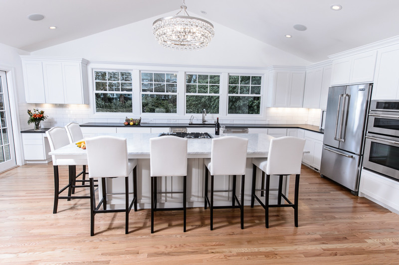 Example of a large classic l-shaped light wood floor eat-in kitchen design in Portland with an undermount sink, recessed-panel cabinets, white cabinets, marble countertops, white backsplash, subway tile backsplash, stainless steel appliances and an island