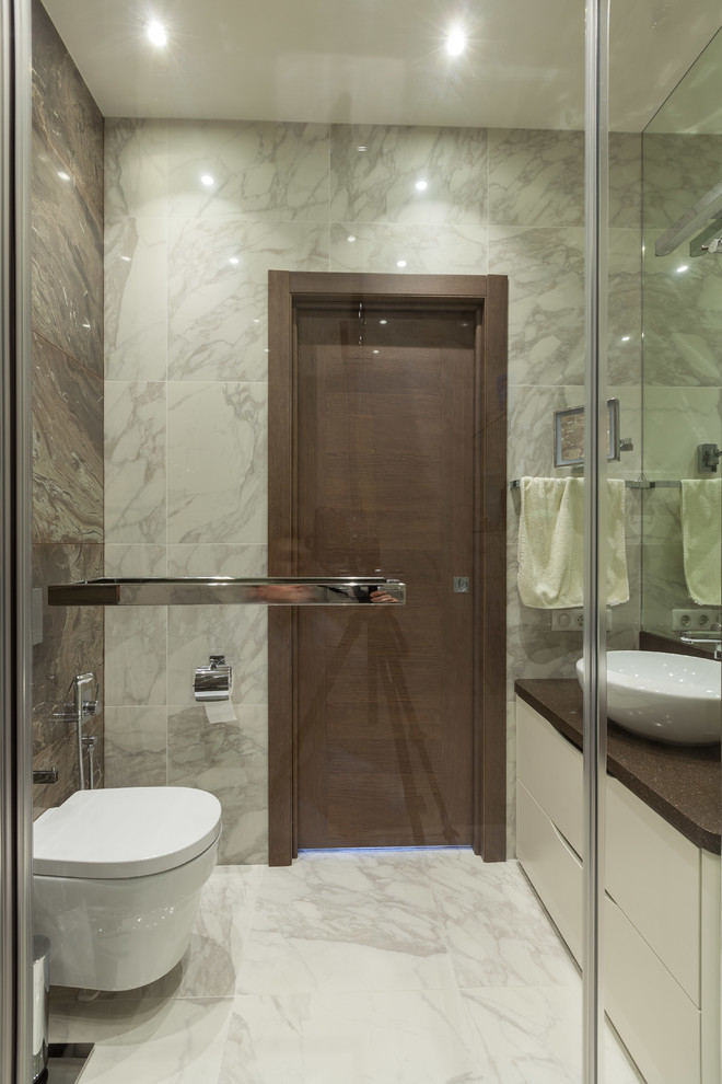 This is an example of a small transitional powder room in Moscow with flat-panel cabinets, white cabinets, a wall-mount toilet, gray tile, porcelain tile, brown walls, porcelain floors, a vessel sink, solid surface benchtops, grey floor and brown benchtops.