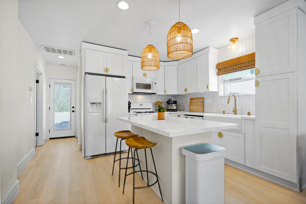 Design ideas for a mid-sized country l-shaped open plan kitchen in Los Angeles with a farmhouse sink, beaded inset cabinets, white cabinets, marble benchtops, white splashback, ceramic splashback, white appliances, vinyl floors, with island, beige floor, white benchtop and vaulted.
