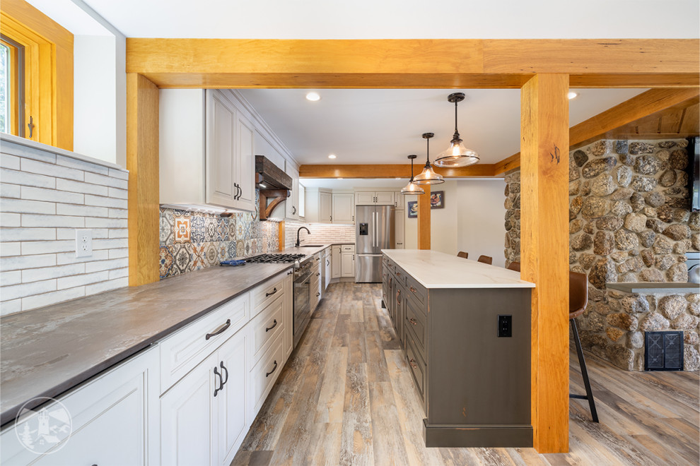 Bild på ett mellanstort rustikt flerfärgad flerfärgat kök, med en undermonterad diskho, luckor med upphöjd panel, vita skåp, vitt stänkskydd, stänkskydd i porslinskakel, rostfria vitvaror, vinylgolv, en köksö och brunt golv