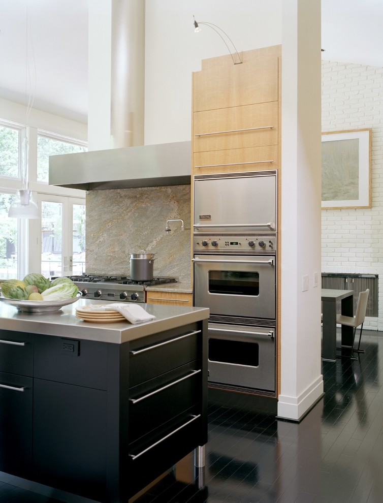 Example of a trendy u-shaped painted wood floor and black floor open concept kitchen design in St Louis with flat-panel cabinets, black cabinets, stainless steel countertops, gray backsplash, stone slab backsplash, stainless steel appliances, a single-bowl sink and an island