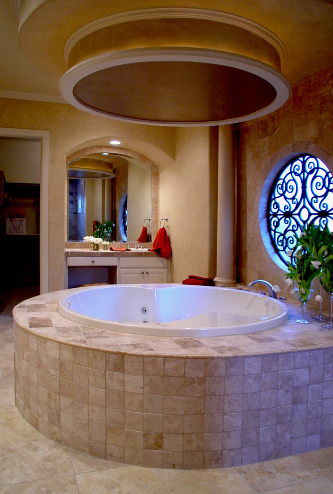 Inspiration for a mediterranean master bathroom in Austin with white cabinets, tile benchtops, a drop-in tub, beige tile, ceramic tile, raised-panel cabinets, brown walls and travertine floors.