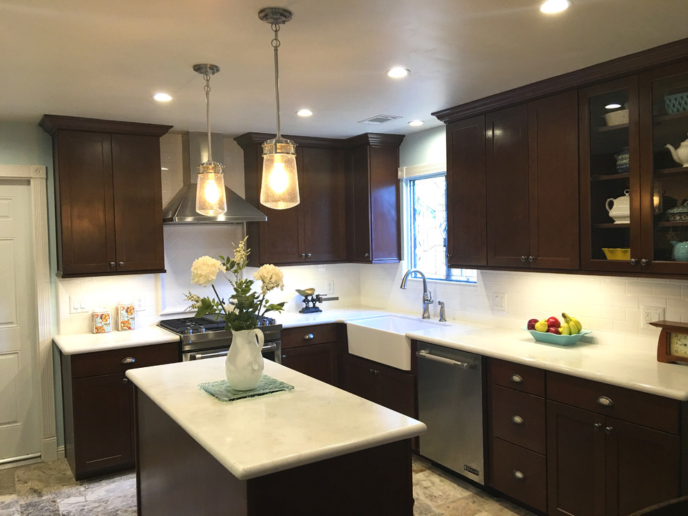 Transitional kitchen photo with a farmhouse sink, shaker cabinets, dark wood cabinets, white backsplash, subway tile backsplash, stainless steel appliances and an island