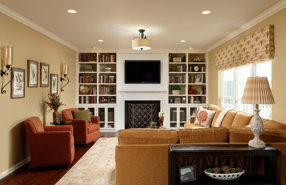 Mid-sized transitional enclosed family room in DC Metro with beige walls, medium hardwood floors, a standard fireplace, a wood fireplace surround, a built-in media wall and brown floor.