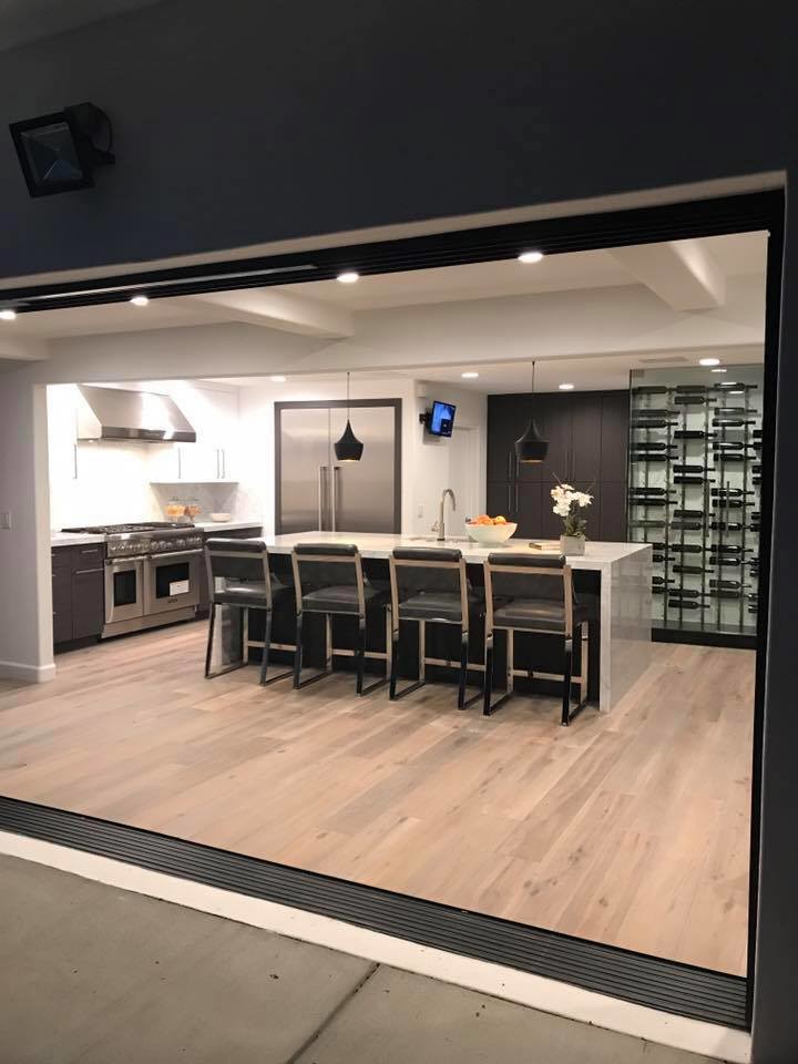 Photo of a mid-sized contemporary single-wall eat-in kitchen in Los Angeles with an undermount sink, flat-panel cabinets, white cabinets, stainless steel appliances, light hardwood floors, with island, brown floor and marble benchtops.