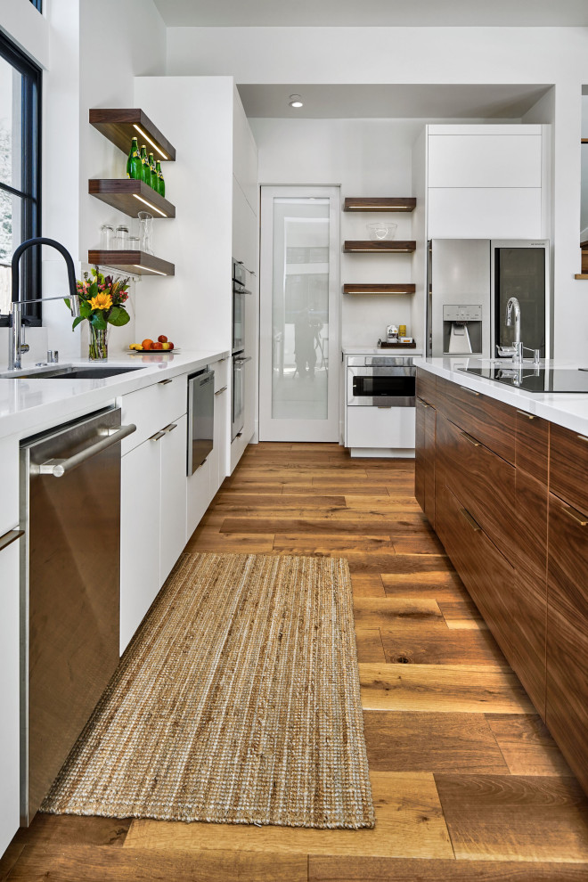 Photo of a large contemporary single-wall eat-in kitchen in San Francisco with an undermount sink, flat-panel cabinets, white cabinets, quartz benchtops, white splashback, stone slab splashback, stainless steel appliances, medium hardwood floors, with island and white benchtop.