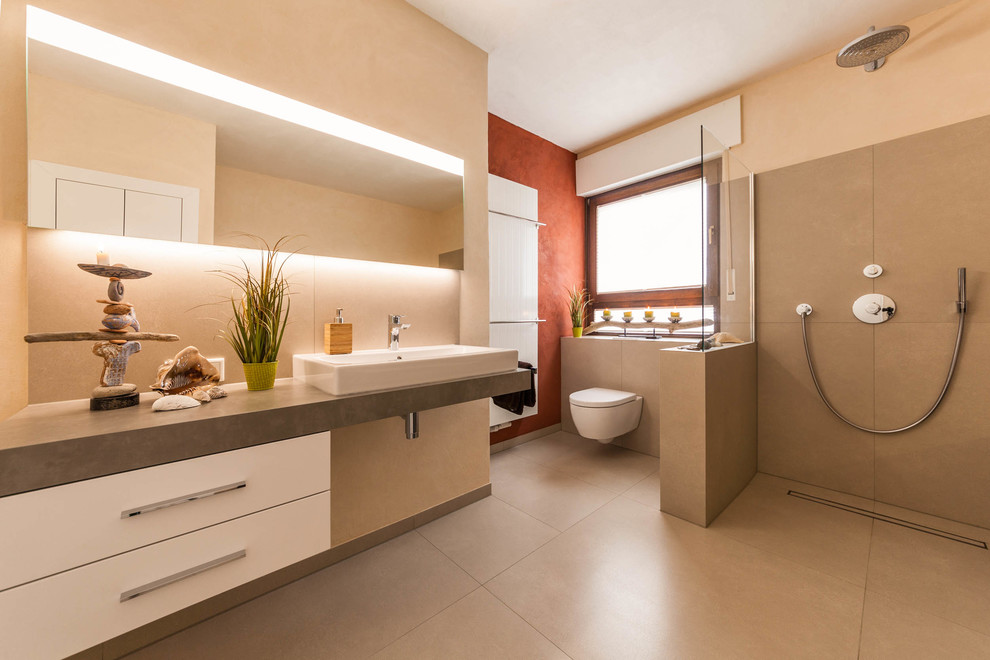 Design ideas for a mid-sized contemporary 3/4 bathroom in Other with flat-panel cabinets, white cabinets, an open shower, a wall-mount toilet, beige tile, cement tile, beige walls, cement tiles, a vessel sink, beige floor and an open shower.