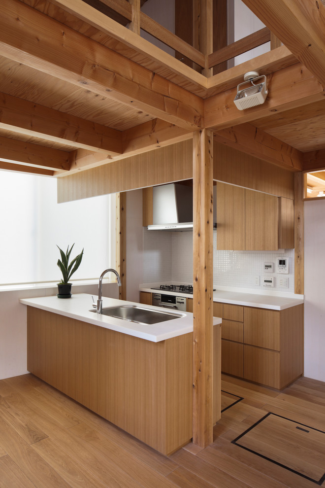 Photo of a contemporary galley kitchen in Tokyo with an undermount sink, flat-panel cabinets, medium wood cabinets, white splashback, mosaic tile splashback, stainless steel appliances, medium hardwood floors, a peninsula, brown floor and white benchtop.