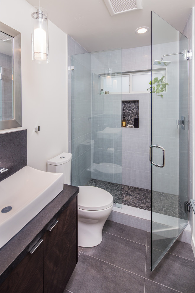 This is an example of a mid-sized contemporary bathroom in San Diego with flat-panel cabinets, dark wood cabinets, an open shower, a one-piece toilet, gray tile, ceramic tile, white walls, porcelain floors, a vessel sink and granite benchtops.