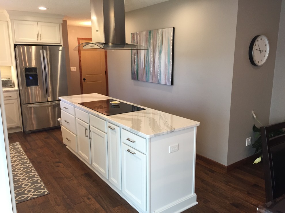 Inspiration for a large transitional l-shaped dark wood floor home design remodel with an undermount sink, flat-panel cabinets, white cabinets, quartz countertops, white backsplash, ceramic backsplash, stainless steel appliances and an island