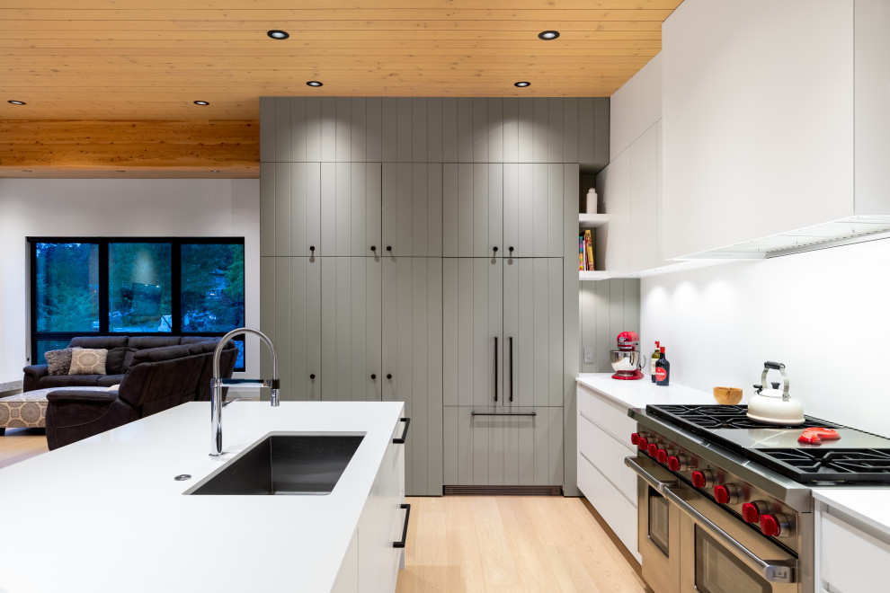 Moderne Wohnküche in L-Form mit grauen Schränken, Küchengeräten aus Edelstahl, hellem Holzboden, Kücheninsel, weißer Arbeitsplatte, Unterbauwaschbecken, flächenbündigen Schrankfronten, beigem Boden, Holzdielendecke und Holzdecke in Vancouver