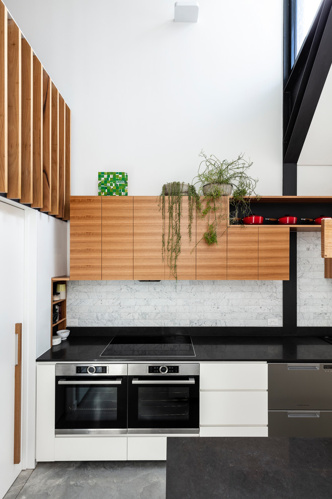 Photo of a mid-sized contemporary eat-in kitchen in Sydney with a double-bowl sink, flat-panel cabinets, white cabinets, quartz benchtops, grey splashback, stainless steel appliances, concrete floors, with island, grey floor and black benchtop.