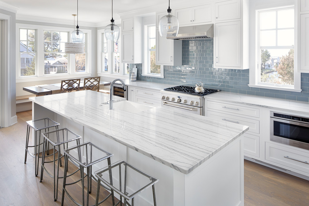 Inspiration for a beach style eat-in kitchen in Other with a farmhouse sink, shaker cabinets, white cabinets, blue splashback, stainless steel appliances, medium hardwood floors, with island, brown floor and grey benchtop.