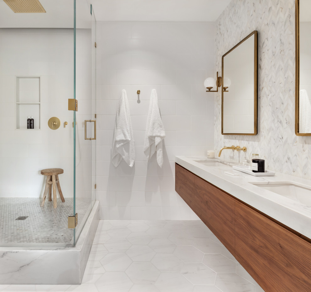 Photo of a scandinavian bathroom in New York with flat-panel cabinets, medium wood cabinets, a corner shower, white tile, white walls, an undermount sink, marble benchtops, white floor, a hinged shower door and white benchtops.