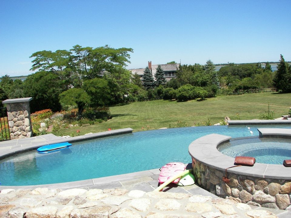 Large mountain style backyard stone and custom-shaped infinity hot tub photo in Boston