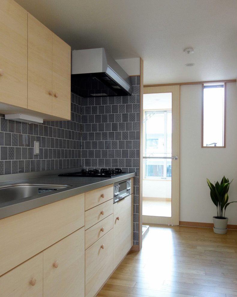 Idéer för små funkis linjära kök med öppen planlösning, med en integrerad diskho, luckor med profilerade fronter, skåp i ljust trä, bänkskiva i rostfritt stål, grått stänkskydd, stänkskydd i porslinskakel, rostfria vitvaror, plywoodgolv och brunt golv