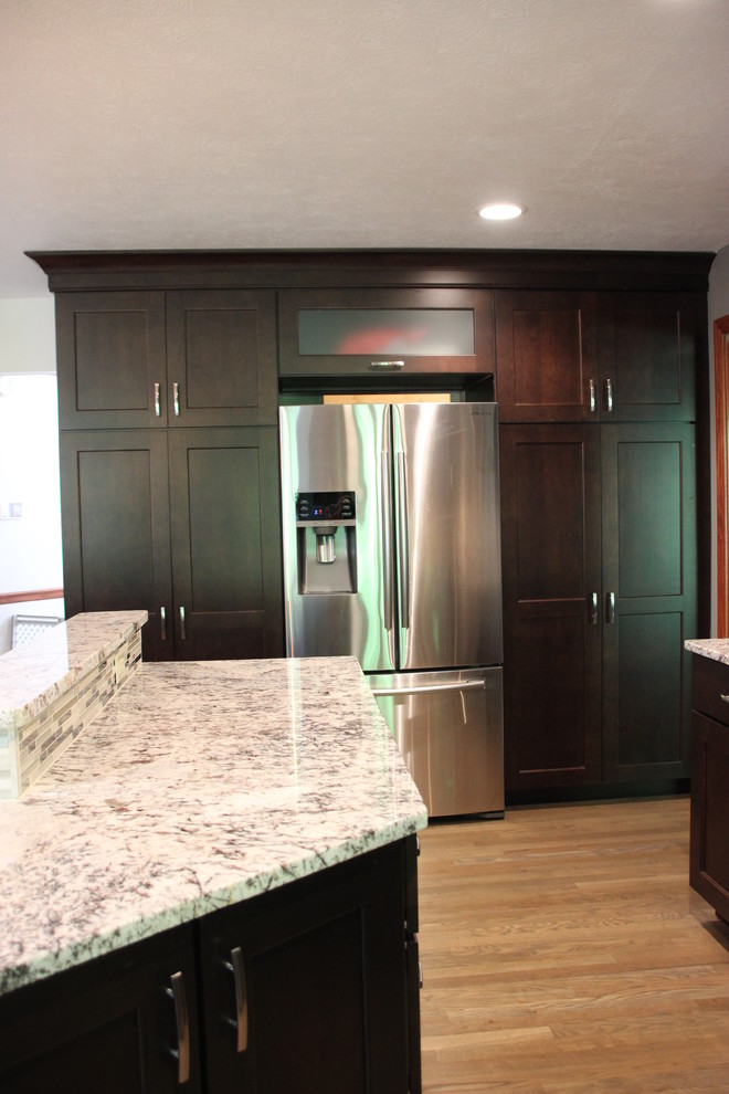 Photo of a large transitional eat-in kitchen in Cleveland with a double-bowl sink, recessed-panel cabinets, dark wood cabinets, granite benchtops, metallic splashback, mosaic tile splashback, stainless steel appliances, light hardwood floors and multiple islands.