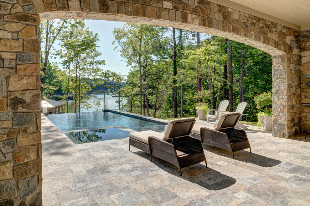 Large country backyard rectangular infinity pool in Charlotte with a hot tub and natural stone pavers.