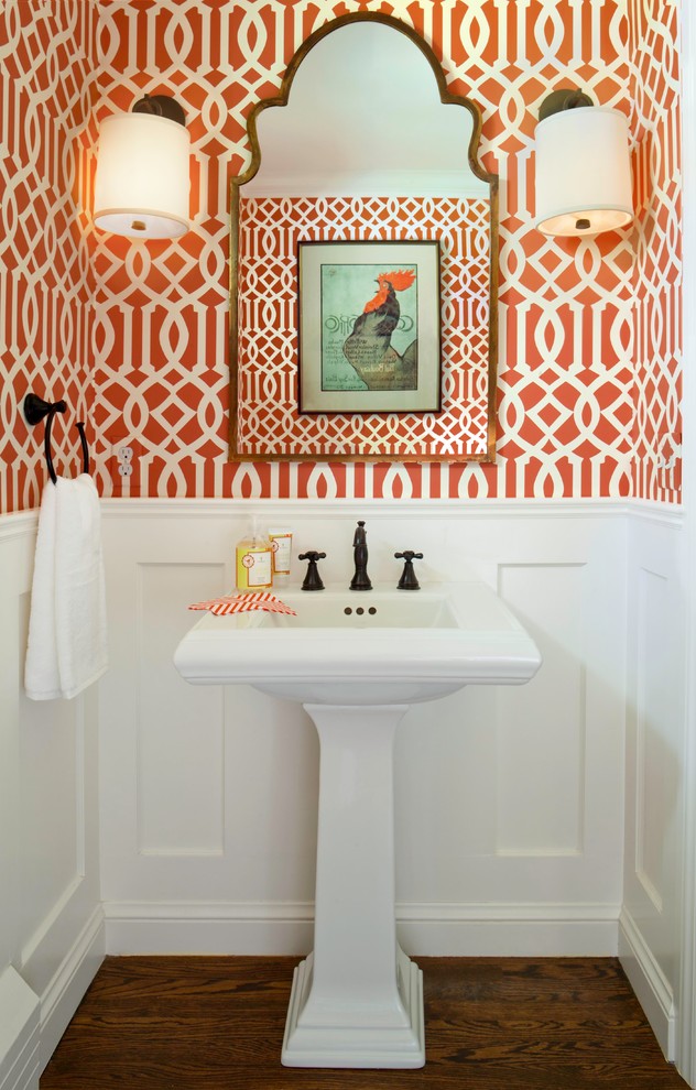 This is an example of a small contemporary powder room in Denver with a pedestal sink, orange walls, dark hardwood floors, a two-piece toilet and brown floor.