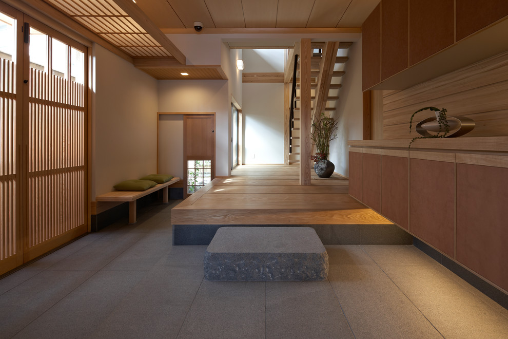 This is an example of a large asian vestibule in Kyoto with white walls, a light wood front door and grey floor.
