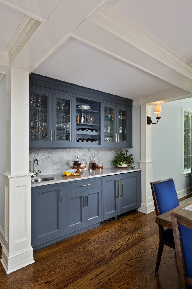 Photo of a mid-sized traditional single-wall wet bar in Boston with an undermount sink, beaded inset cabinets, blue cabinets, marble benchtops, grey splashback, medium hardwood floors, brown floor, grey benchtop and stone slab splashback.