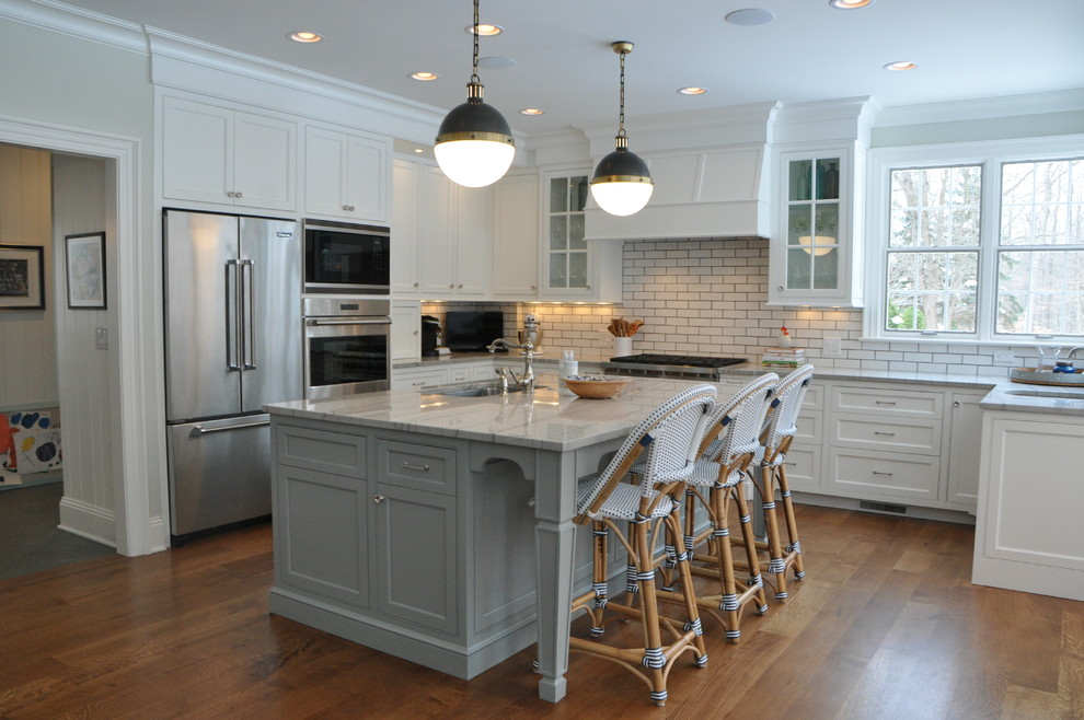 Inspiration for a large transitional l-shaped medium tone wood floor and brown floor open concept kitchen remodel in Cleveland with an undermount sink, recessed-panel cabinets, white cabinets, marble countertops, white backsplash, subway tile backsplash, stainless steel appliances, an island and white countertops