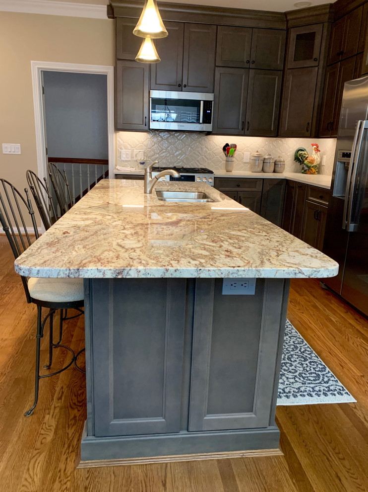 Mid-sized transitional l-shaped medium tone wood floor and brown floor eat-in kitchen photo in Cincinnati with an undermount sink, recessed-panel cabinets, gray cabinets, quartz countertops, white backsplash, porcelain backsplash, stainless steel appliances, an island and white countertops