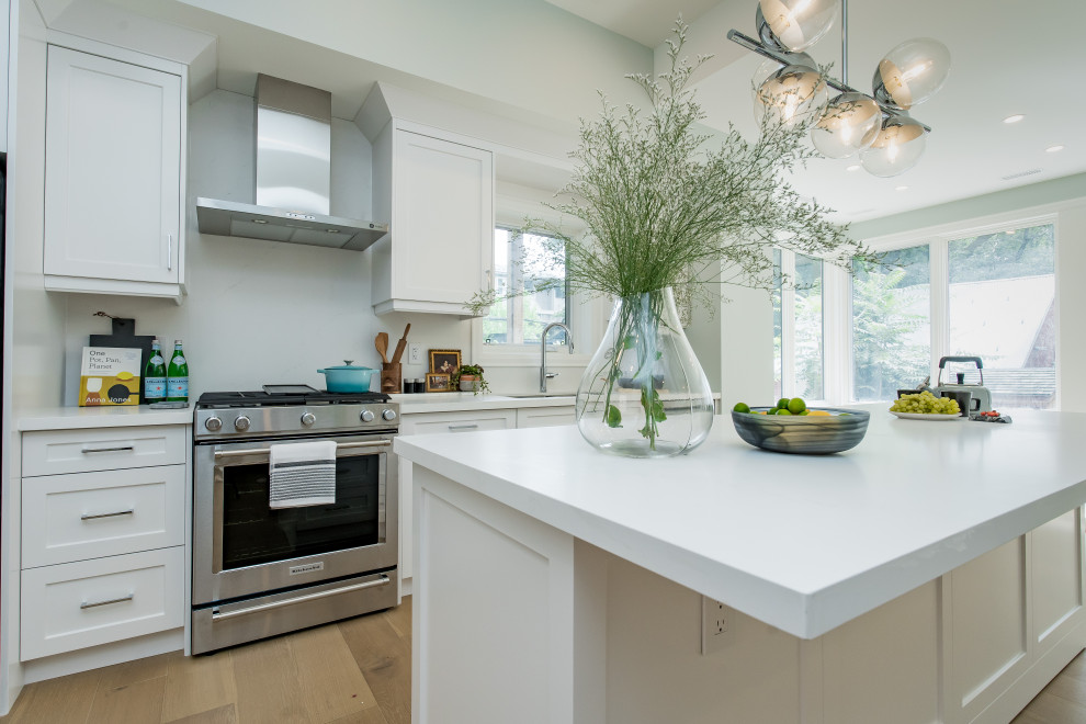 Inspiration for a mid-sized transitional galley light wood floor and beige floor eat-in kitchen remodel in Toronto with a double-bowl sink, shaker cabinets, white cabinets, quartz countertops, white backsplash, quartz backsplash, stainless steel appliances, an island and white countertops