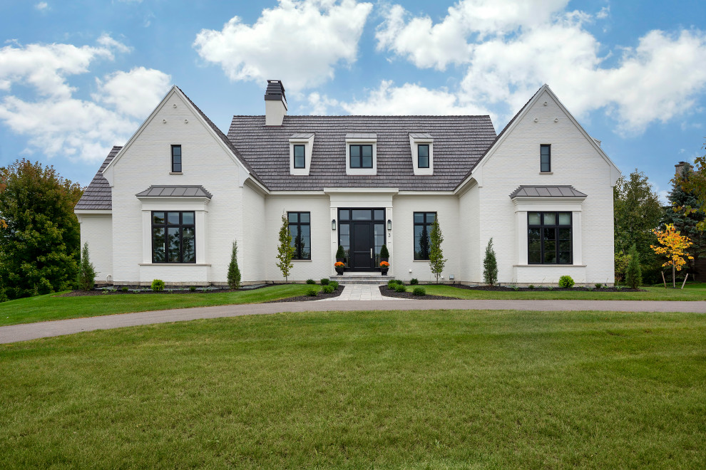 Esempio della villa grande bianca a due piani con rivestimento in mattoni, tetto a capanna, copertura a scandole e tetto bianco