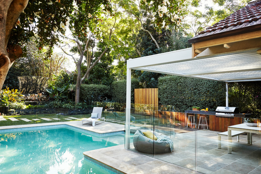 This is an example of a mid-sized contemporary backyard custom-shaped pool in Sydney with natural stone pavers.
