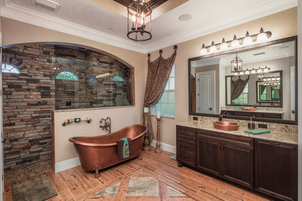 This is an example of a mediterranean master bathroom in Orlando with granite benchtops, recessed-panel cabinets, dark wood cabinets, a claw-foot tub, an alcove shower, beige tile, brown tile, gray tile, stone tile, beige walls, light hardwood floors, a drop-in sink, orange floor and an open shower.