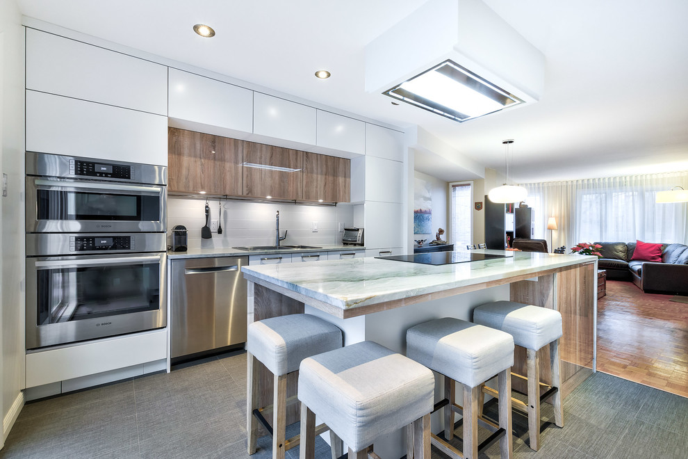 Mid-sized contemporary open plan kitchen in Montreal with flat-panel cabinets, white cabinets, quartz benchtops, white splashback, ceramic splashback, stainless steel appliances, porcelain floors, with island and grey floor.