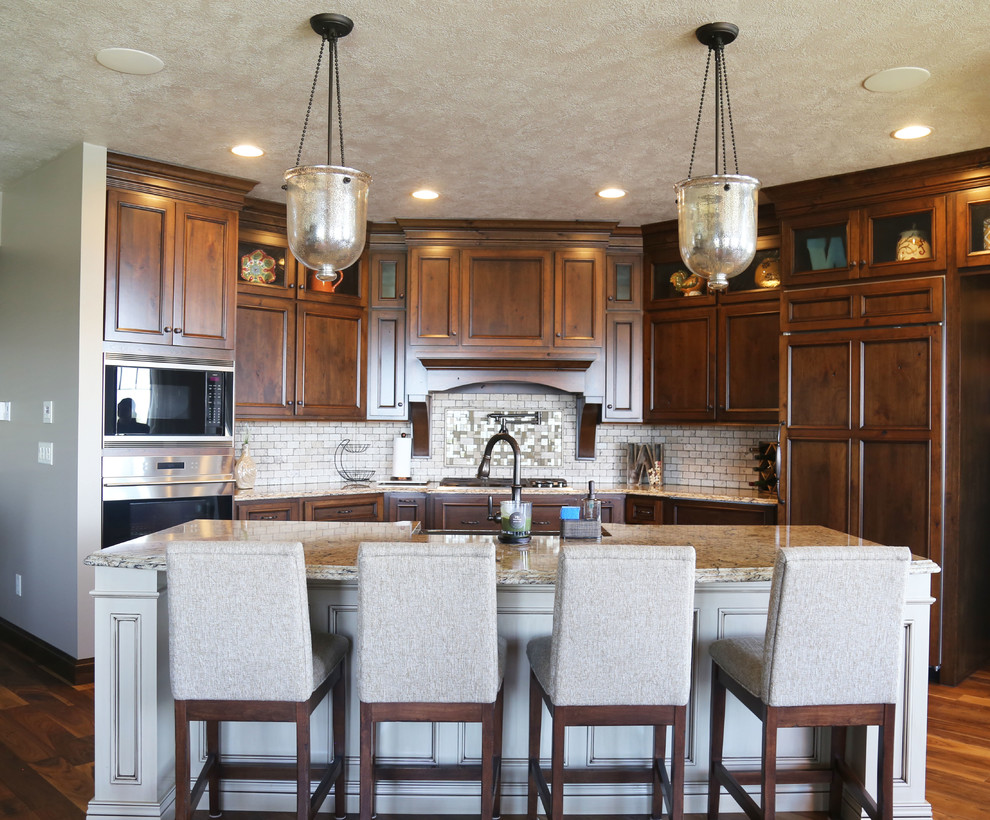 Inspiration for a mid-sized transitional l-shaped medium tone wood floor eat-in kitchen remodel with a farmhouse sink, recessed-panel cabinets, medium tone wood cabinets, granite countertops, beige backsplash, stone tile backsplash, stainless steel appliances and an island