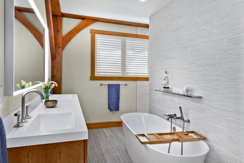 Foto på ett stort amerikanskt vit en-suite badrum, med släta luckor, bruna skåp, ett fristående badkar, en kantlös dusch, en toalettstol med separat cisternkåpa, grå kakel, stenkakel, vita väggar, kalkstensgolv, ett integrerad handfat, bänkskiva i akrylsten, grått golv och med dusch som är öppen