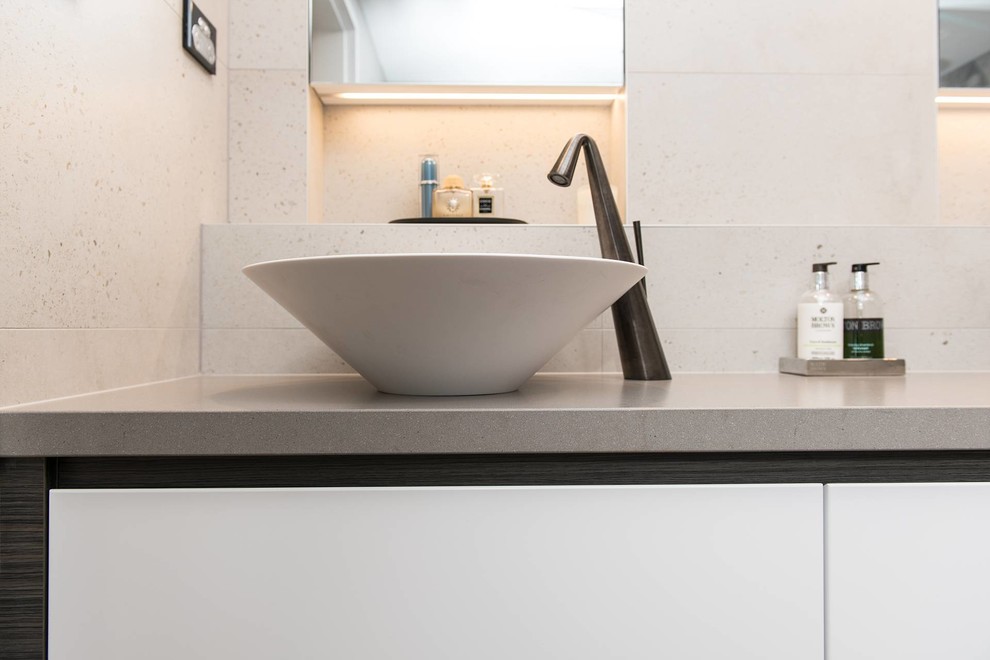 This is an example of a large industrial master bathroom in Sydney with flat-panel cabinets, white cabinets, an open shower, a one-piece toilet, stone slab, porcelain floors, a vessel sink, an open shower, beige tile, beige walls, engineered quartz benchtops, brown floor, beige benchtops, a niche and a double vanity.