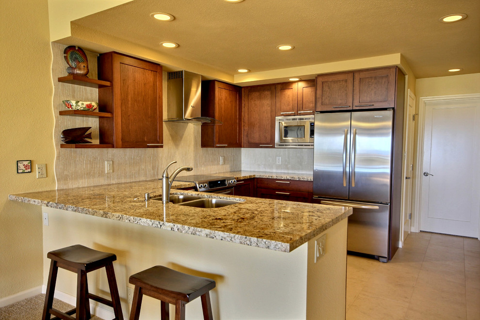 Photo of a mid-sized tropical u-shaped eat-in kitchen in Hawaii with a double-bowl sink, shaker cabinets, medium wood cabinets, granite benchtops, beige splashback, stone tile splashback, stainless steel appliances, porcelain floors and no island.