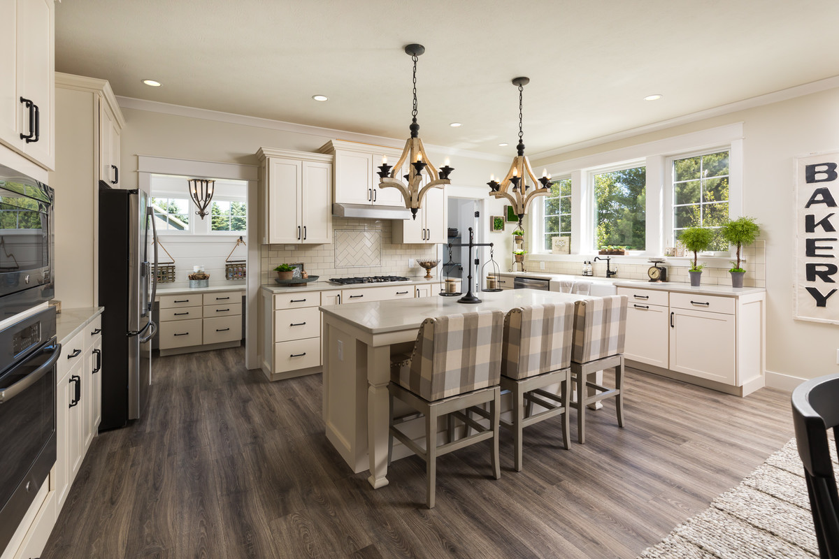 Design ideas for a traditional eat-in kitchen in Grand Rapids with a farmhouse sink, shaker cabinets, beige cabinets, beige splashback, subway tile splashback, stainless steel appliances, dark hardwood floors, with island and brown floor.