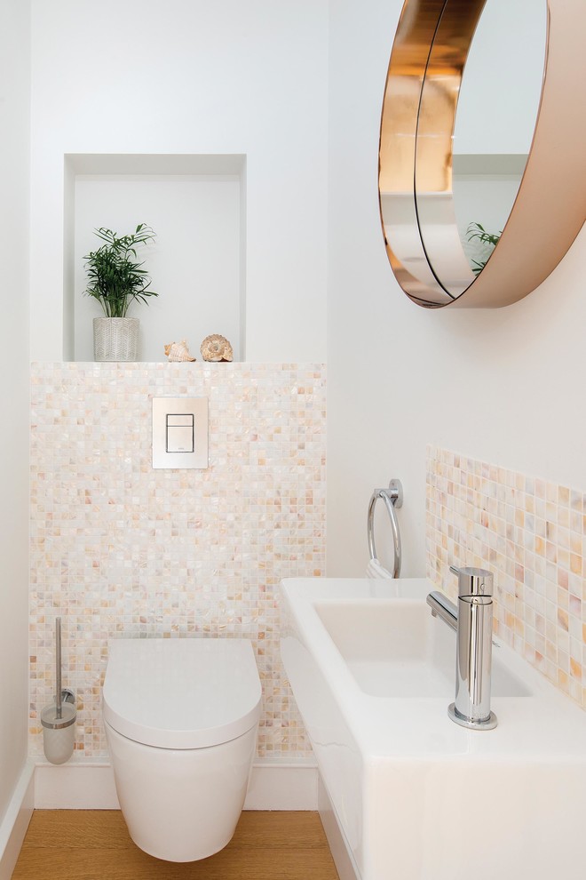 Small transitional powder room in London with a wall-mount toilet, beige tile, mosaic tile, white walls, a wall-mount sink and light hardwood floors.