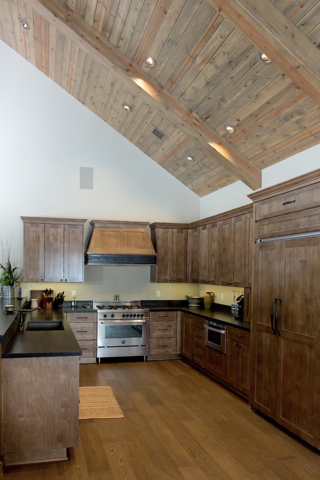 Large mountain style u-shaped medium tone wood floor and brown floor open concept kitchen photo in Phoenix with an undermount sink, shaker cabinets, medium tone wood cabinets, solid surface countertops, paneled appliances, no island and black countertops