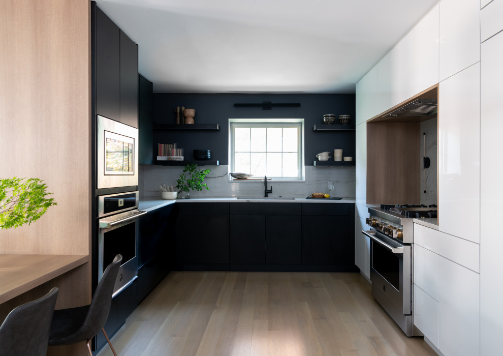Cette image montre une cuisine design avec un évier encastré, un placard à porte plane, des portes de placard noires, une crédence blanche, un électroménager en acier inoxydable et parquet clair.