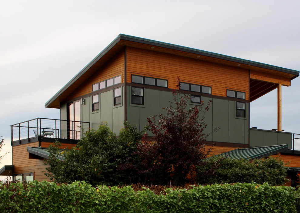 Expansive midcentury three-storey green house exterior in Seattle with concrete fiberboard siding, a shed roof and a metal roof.