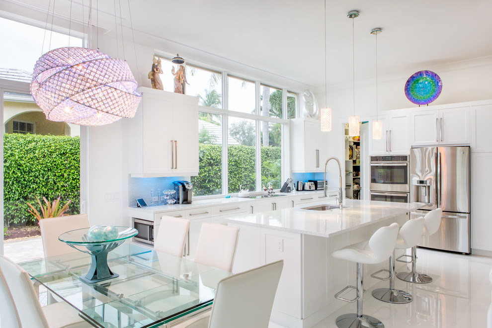 Large contemporary l-shaped open plan kitchen in Miami with an undermount sink, flat-panel cabinets, white cabinets, quartz benchtops, white splashback, glass tile splashback, stainless steel appliances, porcelain floors and with island.