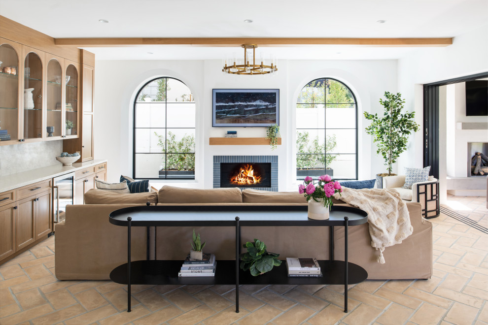 Example of a mid-sized tuscan open concept terra-cotta tile and beige floor family room design in Los Angeles with white walls, a standard fireplace, a tile fireplace and a wall-mounted tv
