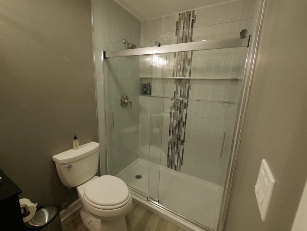 Photo of a mid-sized transitional 3/4 bathroom in Chicago with black cabinets, an alcove shower, a two-piece toilet, gray tile, matchstick tile, grey walls, laminate floors, tile benchtops, grey floor, a sliding shower screen and black benchtops.