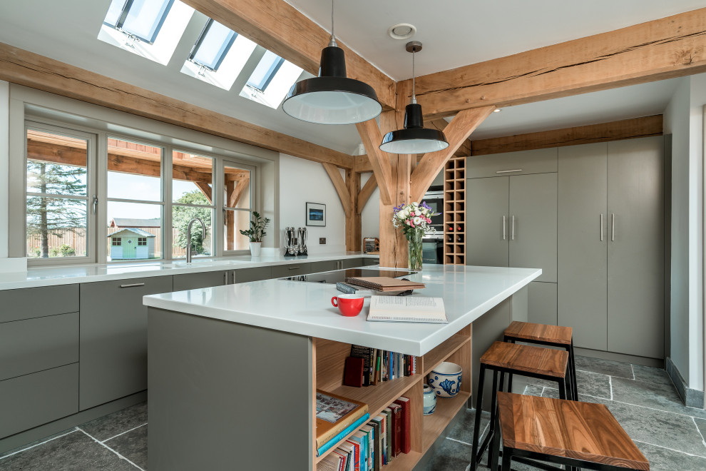 This is an example of a farmhouse l-shaped kitchen with flat-panel cabinets, grey cabinets, integrated appliances, an island, grey floors and white worktops.