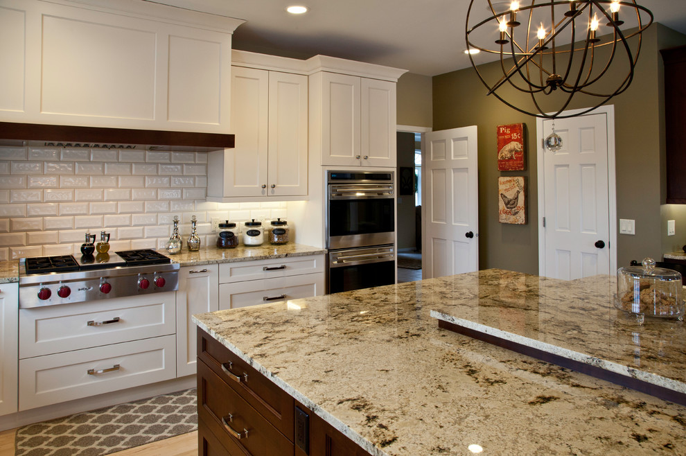 Large transitional l-shaped light wood floor and brown floor open concept kitchen photo with an undermount sink, shaker cabinets, white cabinets, granite countertops, white backsplash, subway tile backsplash, paneled appliances and an island