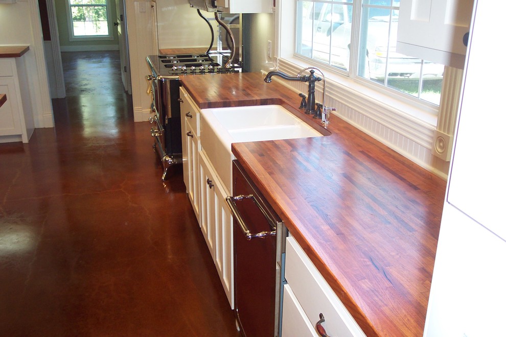This is an example of a mid-sized country galley eat-in kitchen in Austin with a farmhouse sink, flat-panel cabinets, white cabinets, wood benchtops, white splashback, timber splashback, coloured appliances, concrete floors, with island, brown floor and brown benchtop.