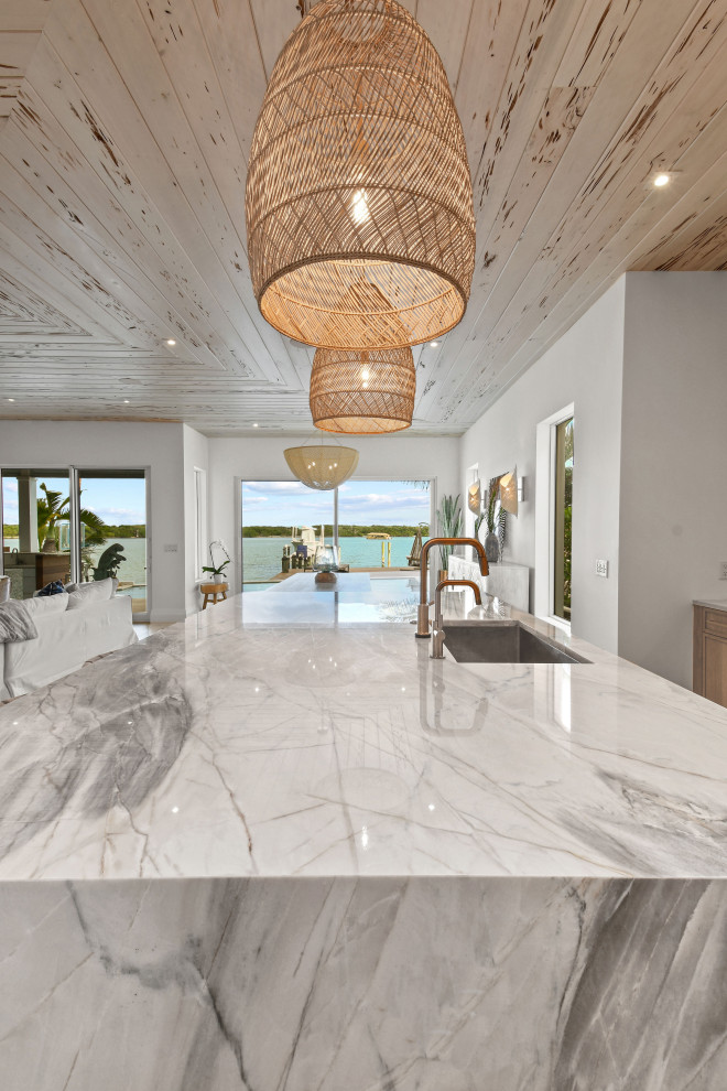This is an example of a mid-sized beach style l-shaped open plan kitchen in Other with distressed cabinets, quartzite benchtops, panelled appliances and with island.